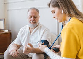 A healthcare professional checks an elderly man's blood pressure in a cozy room.