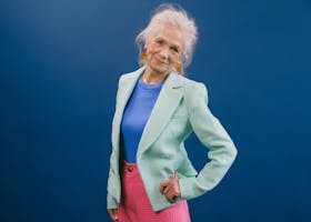 Confident senior woman in stylish pastel attire, showcasing fashion on a blue background.