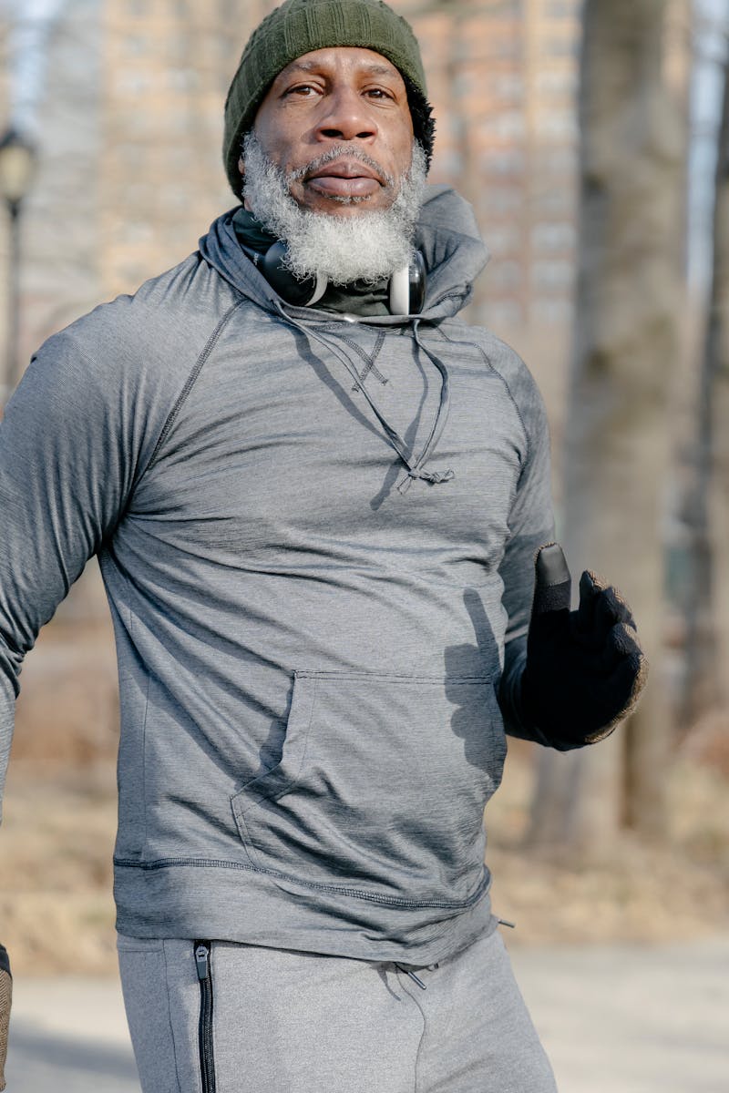 Elderly man exercising outdoors in winter, wearing gray sweater and beanie.